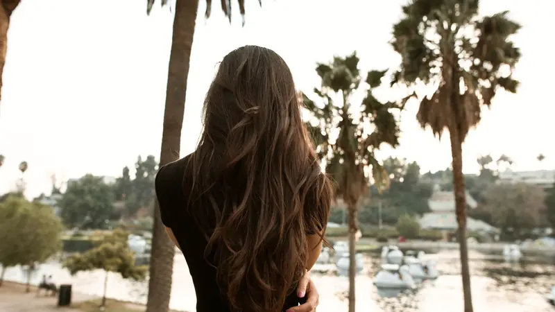 Femme vue de dos aux longs cheveux bruns ondulés éclaircis de reflets plus clairs sur les longueurs
