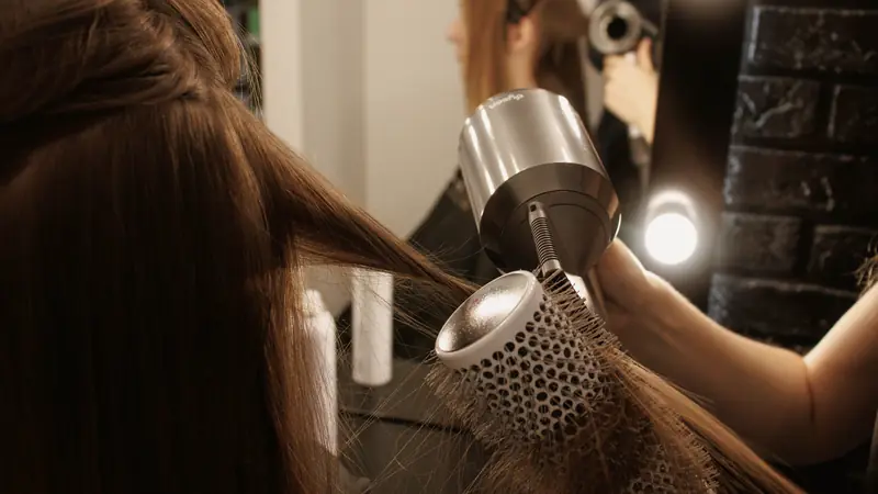 Femme qui sèche ses cheveux avec une brosse ronde et un sèche-cheveux