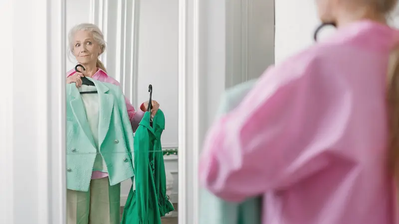 Femme aux cheveux blancs qui choisit un vêtement devant un miroir
