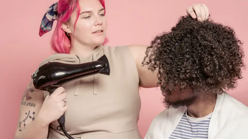 Coiffeuse qui sèche au sèche-cheveux une chevelure très bouclée
