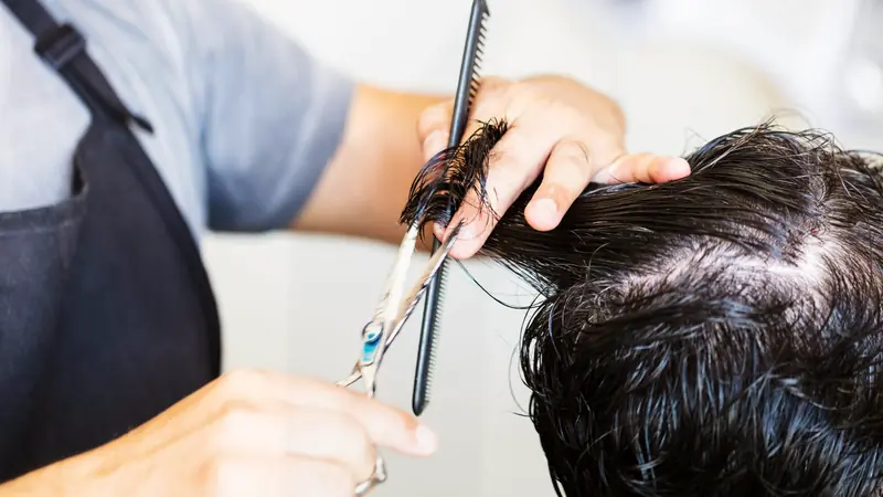 Coiffeur qui coupe une chevelure brune épaisse aux ciseaux