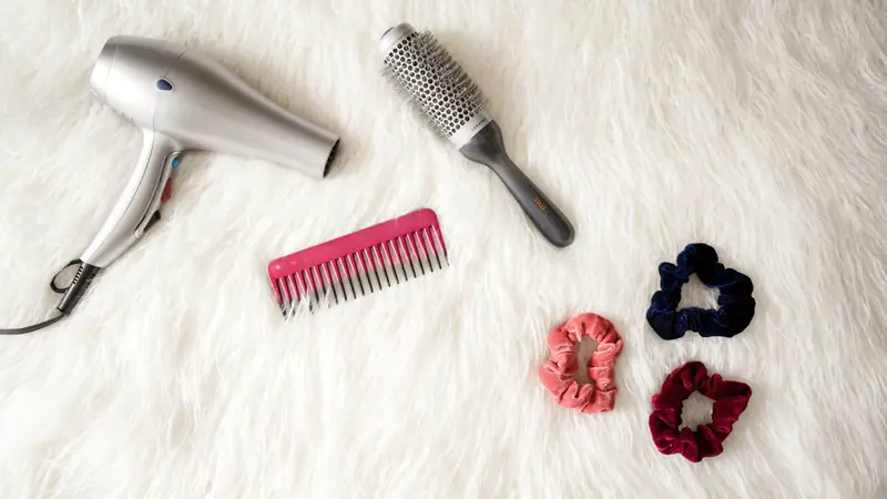 Sèche-cheveux, brosse ronde, peigne et chouchous sur un tapis blanc