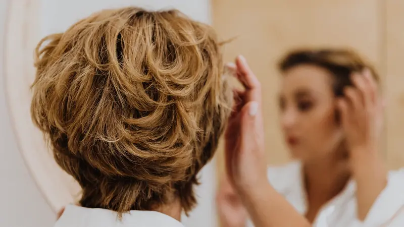 Femme aux cheveux courts qui se coiffe devant un miroir