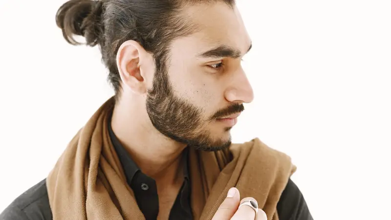 Homme barbu de profil, cheveux bruns relevés en petit chignon à l'arrière du crâne