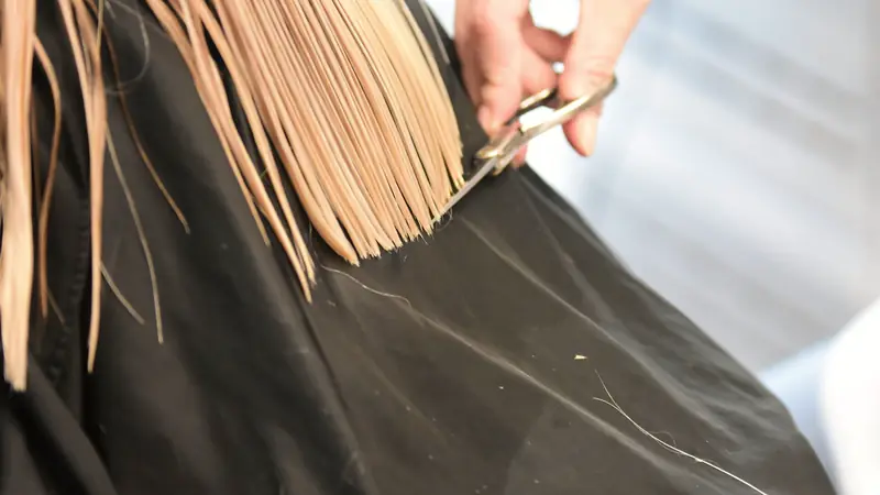 Coiffeur qui coupe aux ciseaux les pointes de cheveux blonds