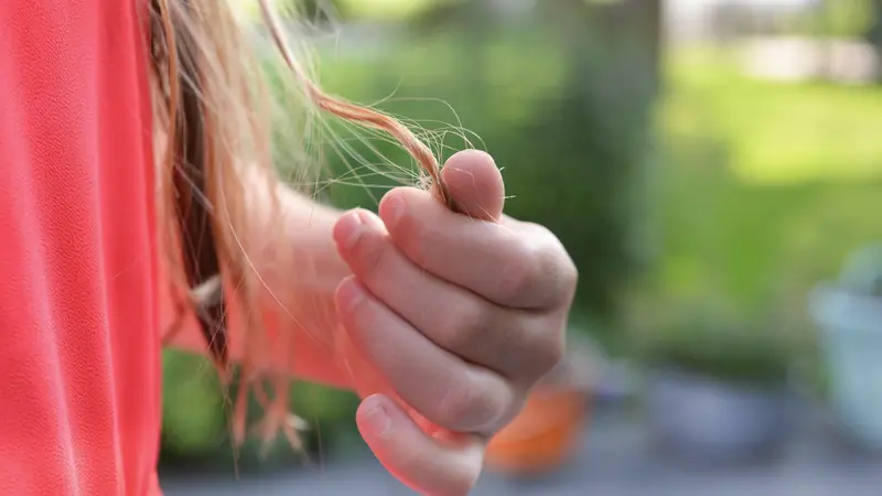Main qui tient des pointes de cheveux longs, en extérieur