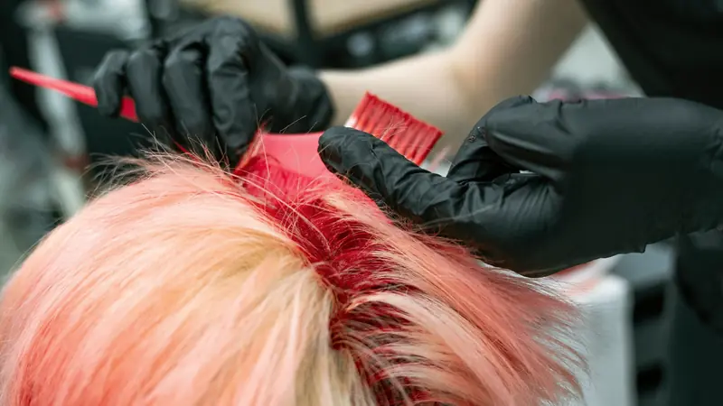 Coloriste qui applique une couleur rose au pinceau sur des racines