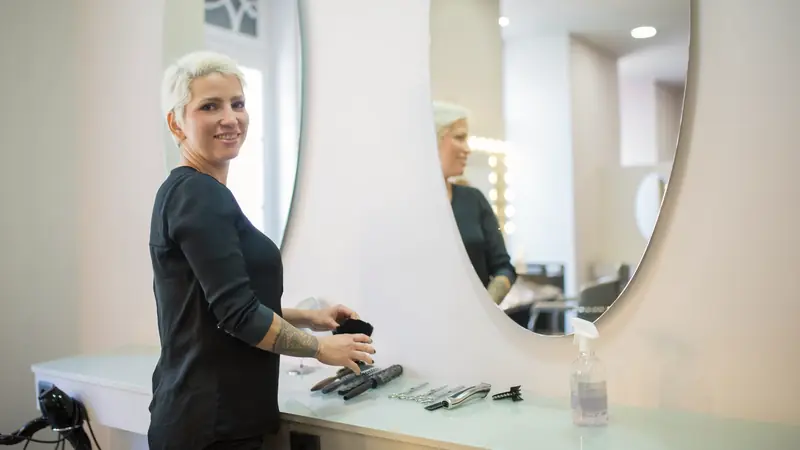 Coiffeuse souriante devant un grand miroir rond dans un salon
