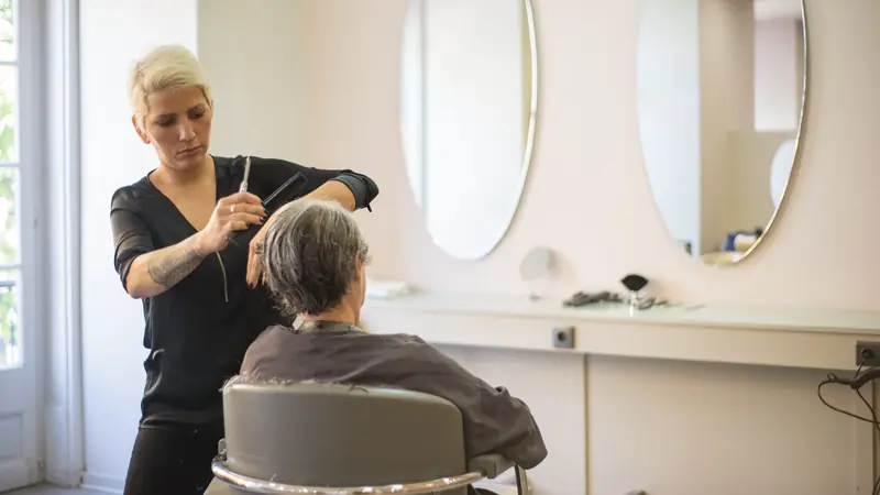 Coiffeuse qui coupe les cheveux gris d'une cliente dans un salon lumineux