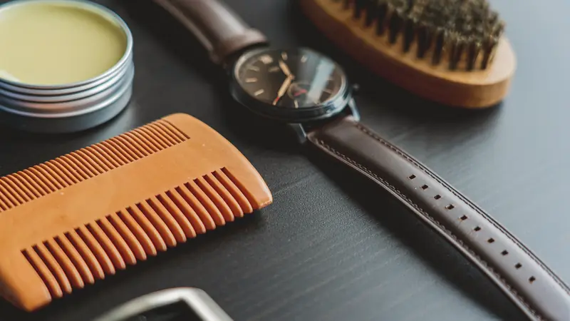 Boîte métallique ouverte de cire jaune posée près d'un peigne en bois, d'une brosse et d'une montre