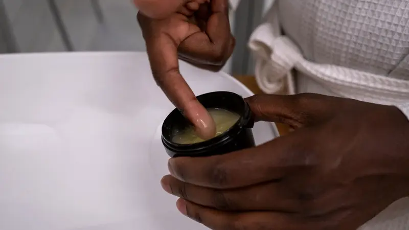 Index plongé dans un pot noir de produit coiffant tenu au-dessus d'un lavabo blanc