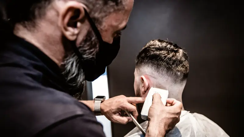 Coiffeur réalisant un dégradé à la tondeuse sur le côté de la tête d'un client