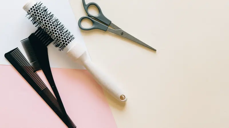 Ciseaux, peignes noirs et brosse ronde posés sur un fond pastel rose et crème