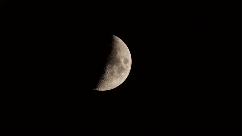 Lune proche du premier quartier, cratères visibles, sur un ciel nocturne noir