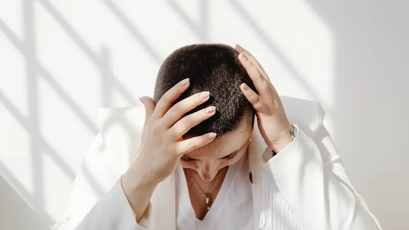 Personne aux cheveux très courts, tête baissée, les deux mains posées sur le crâne