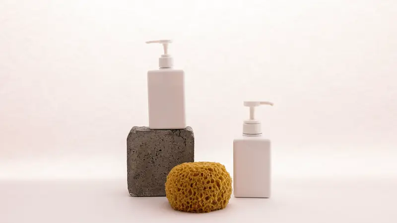 Flacons pompe de soins et éponge naturelle sur fond clair