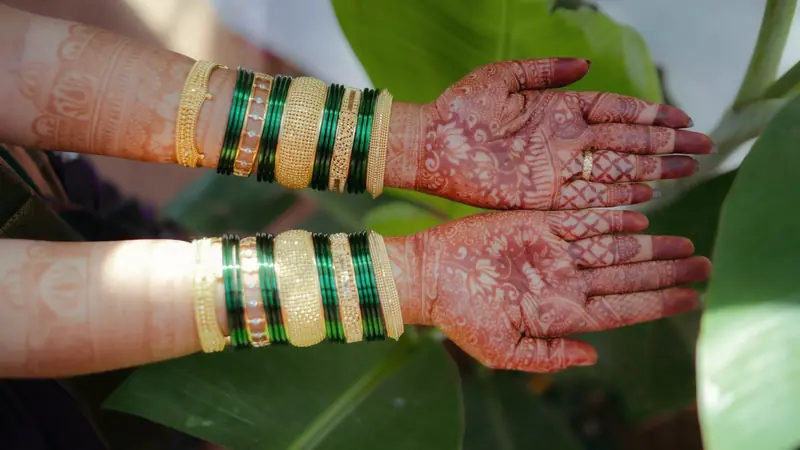 Deux mains ornées de motifs brun-rouge au henné traditionnel, poignets couverts de bracelets dorés et verts