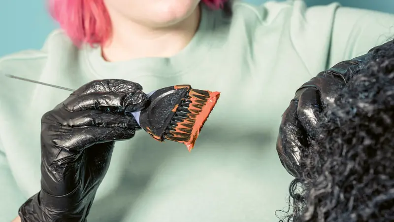 Mains gantées qui appliquent un produit au pinceau sur des cheveux bouclés