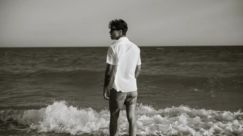 Homme vu de dos face à la mer, cheveux courts décoiffés et texturés sur le dessus, photo en noir et blanc