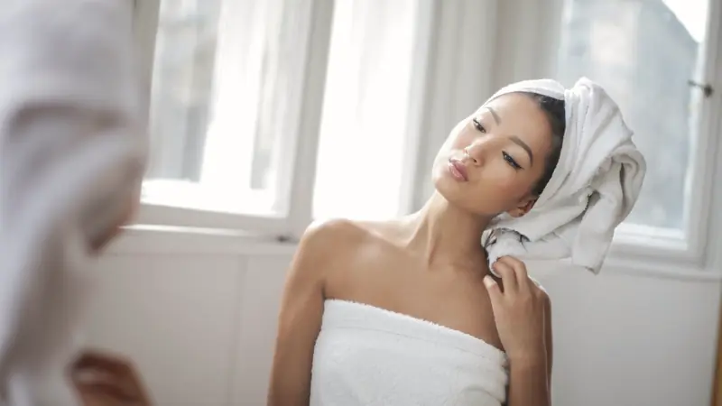 Femme qui sèche ses cheveux avec une serviette près d'une fenêtre