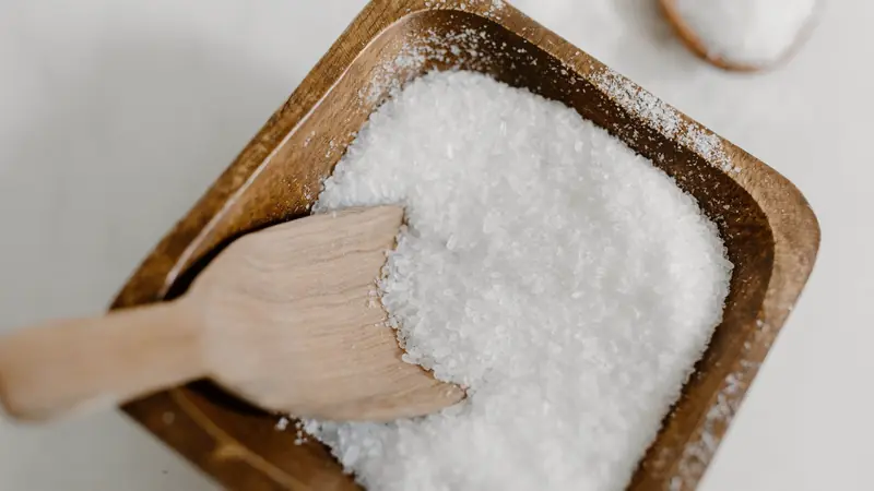 Gros sel blanc dans un bol carré en bois avec une spatule en bois