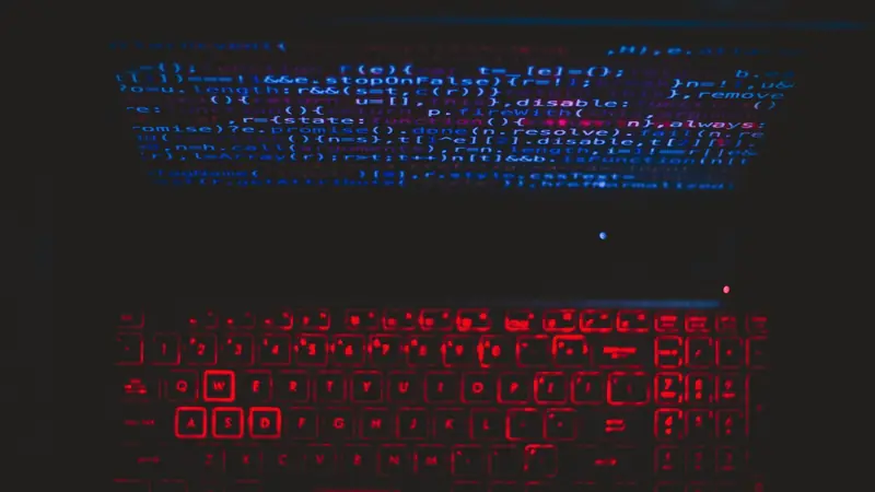 Ordinateur portable dans le noir, lignes de code bleues à l'écran et clavier rétroéclairé en rouge